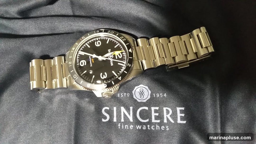 A close-up shot of a Bell & Ross GMT watch with a black dial and a stainless steel bracelet. The watch is placed on a black cloth with the SINCERE fine watches logo. The bezel has 24-hour markings.