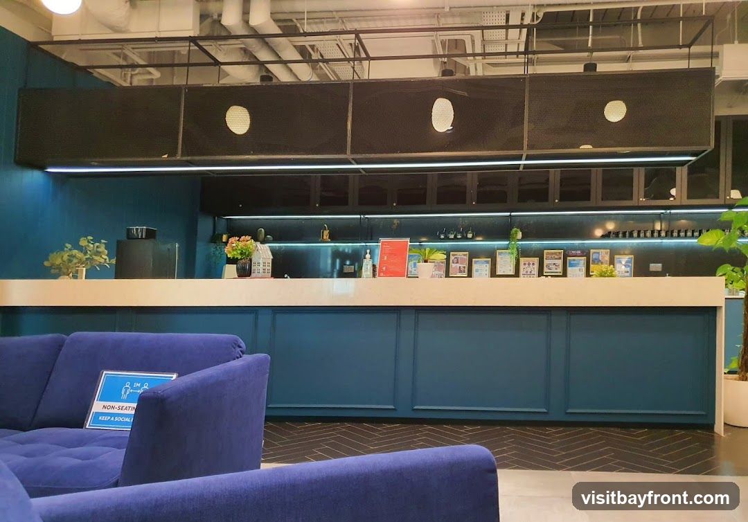 A modern reception area with a blue counter and blue sofas. There are several framed pictures and documents displayed on the counter. A sign on the sofa indicates "NON-SEATING KEEP A SOCIAL DISTANCE".
