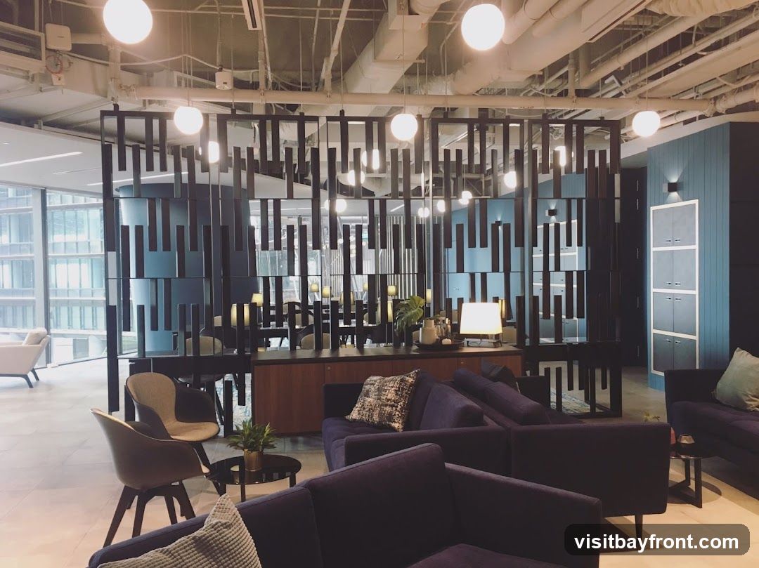 A contemporary lounge area with dark blue sofas, accent chairs, and a decorative room divider. The space features industrial-style lighting and a large window with a view of a city skyline.