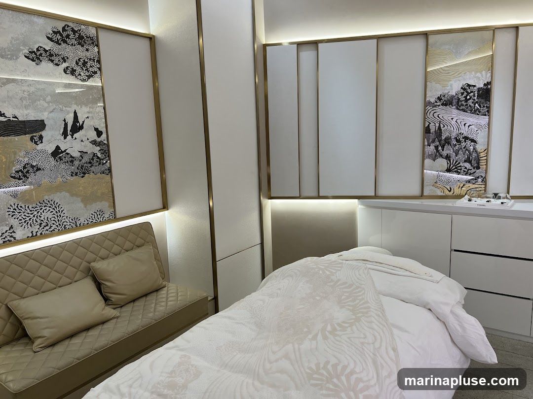A serene spa treatment room with a massage bed covered in white linens, a tufted beige sofa with pillows, and decorative wall panels featuring abstract nature-inspired artwork. The room is illuminated by soft, ambient lighting.