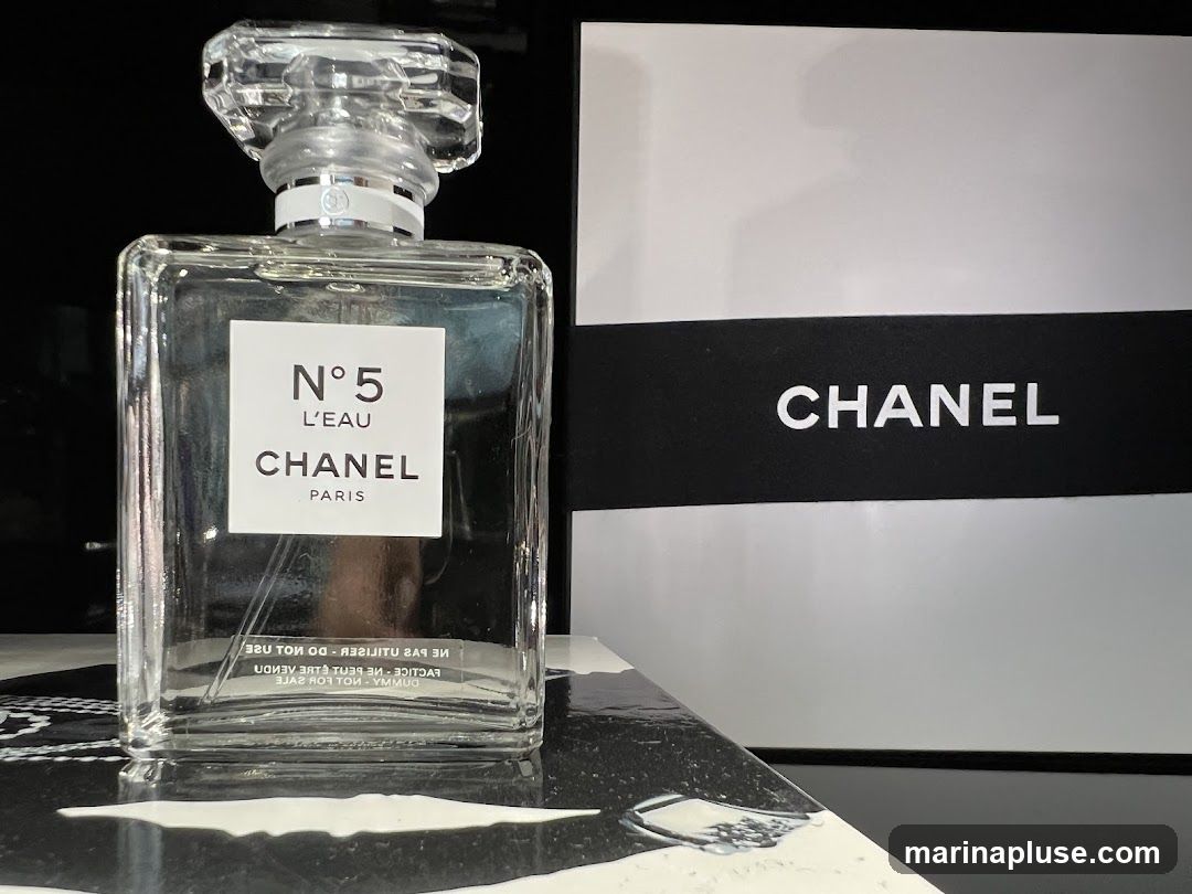 A clear glass bottle of Chanel No. 5 L'Eau perfume is displayed next to a white and black Chanel box. The bottle has a white label with black text that reads "N°5 L'EAU CHANEL PARIS". The box has a black band with the word "CHANEL" printed in white.