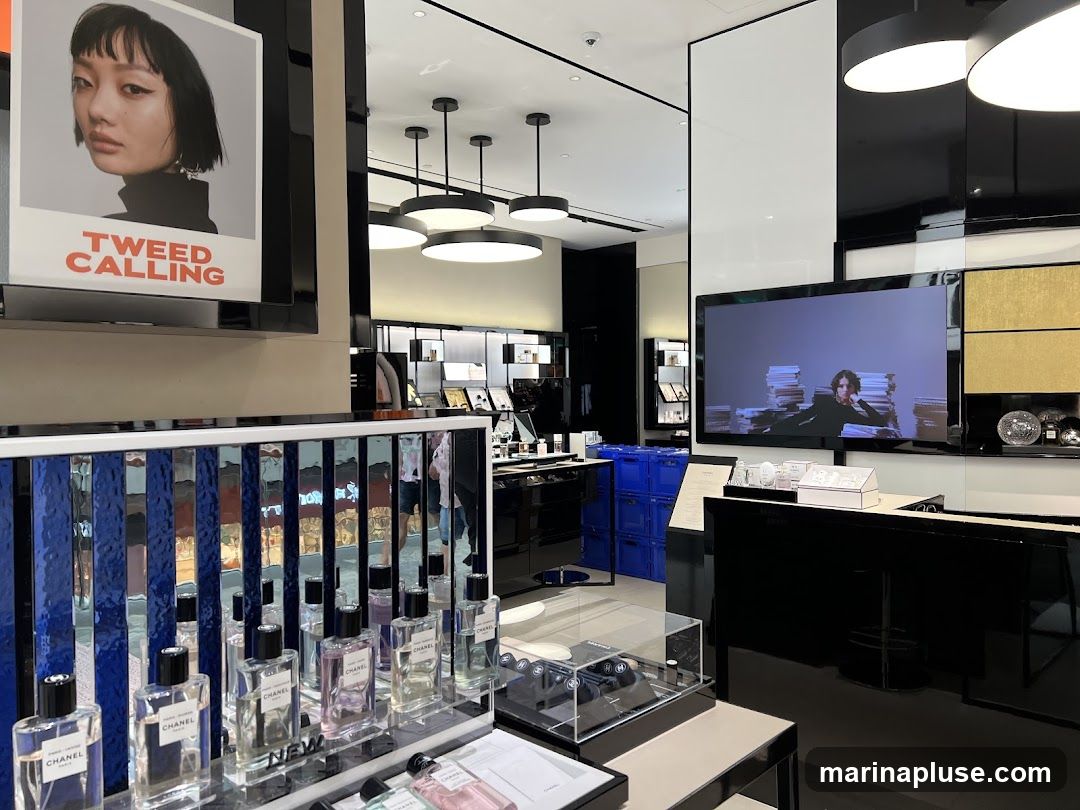 A display of Chanel perfumes in a store. A large screen shows a video, and a poster with the text "TWEED CALLING" is visible.