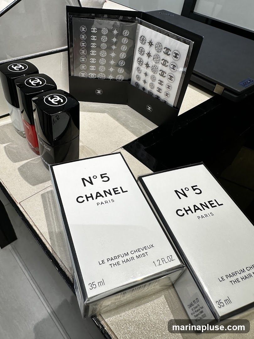A display of Chanel beauty products, including two boxes of N°5 Le Parfum Cheveux The Hair Mist, four bottles of nail polish, and two sets of decorative nail stickers, all featuring the Chanel logo.