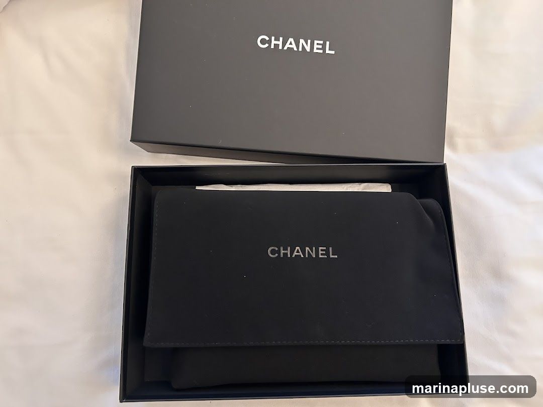 A black Chanel box is open, revealing a black pouch inside. The Chanel logo is visible on both the box and the pouch.