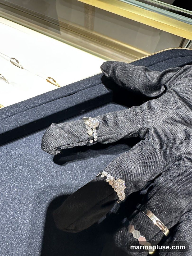 A gloved hand displays several diamond rings in a jewelry store display case. The rings are set with various diamonds and have intricate band designs.