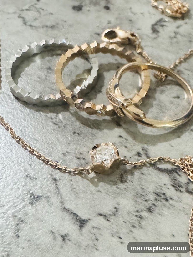 A close-up shot of several pieces of jewelry, including rings and a necklace, laid out on a marbled surface. The jewelry appears to be made of gold and features diamonds.