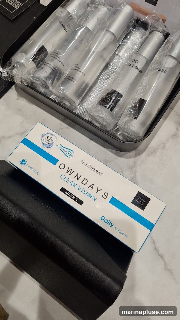 A box of OWNDAYS CLEAR VISION ADVANCE daily contact lenses is shown, along with a case containing several bottles of glasses cleaner. The contact lens box indicates 45% water content, 55% silicone hydrogel, and UV blocking. The glasses cleaner bottles are individually wrapped.