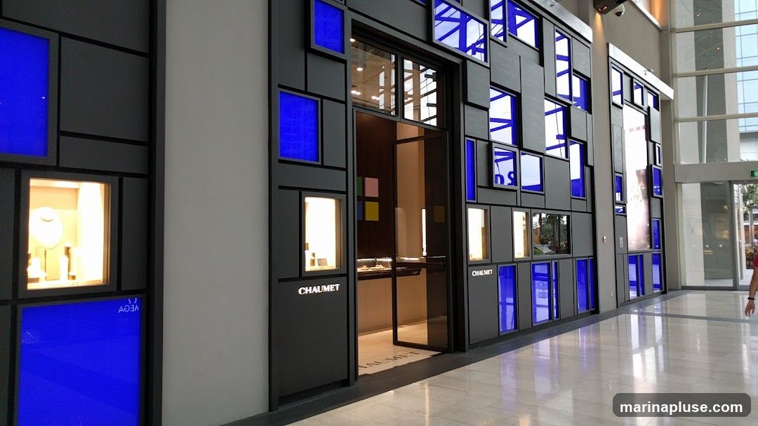 The exterior of a modern jewelry store with a black facade decorated with numerous blue and illuminated display windows. The store's name,