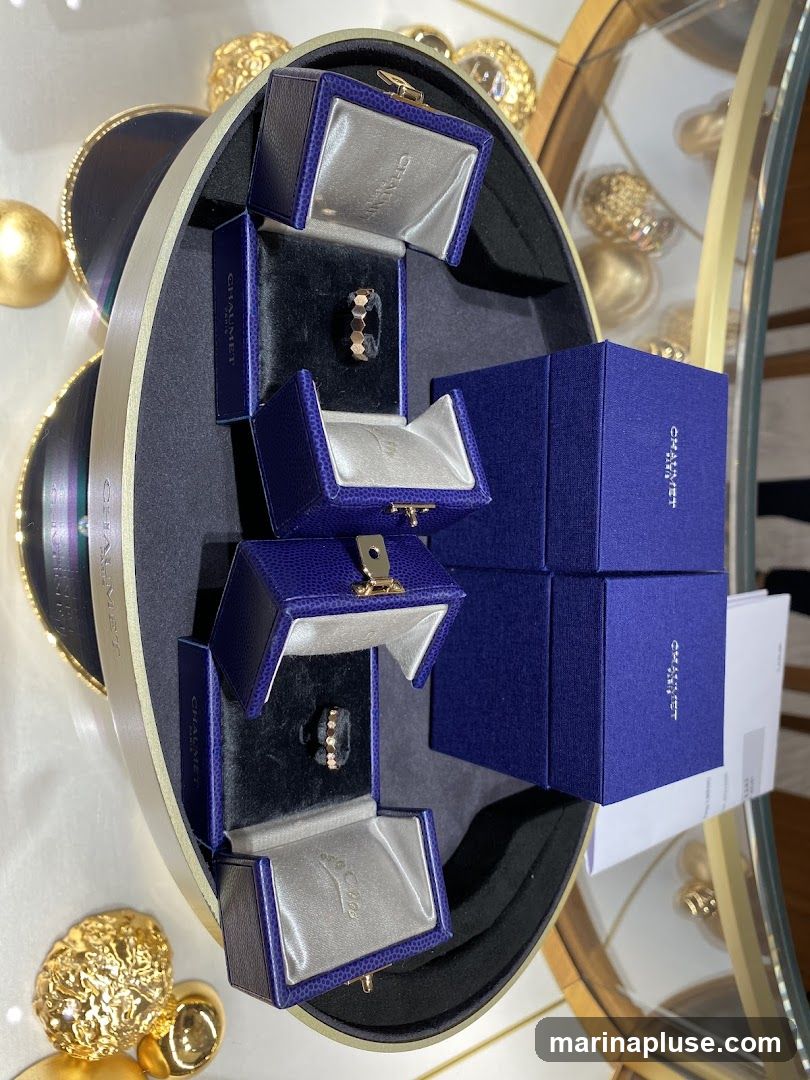 A display of rings in blue velvet-lined boxes with gold clasps. The boxes are branded with the name CHAUMET. Some boxes are open, revealing rose gold rings, one with small diamonds. The display is set within a larger oval tray with a gold trim. In the background, there are decorative gold objects and a mirror reflecting more jewelry.