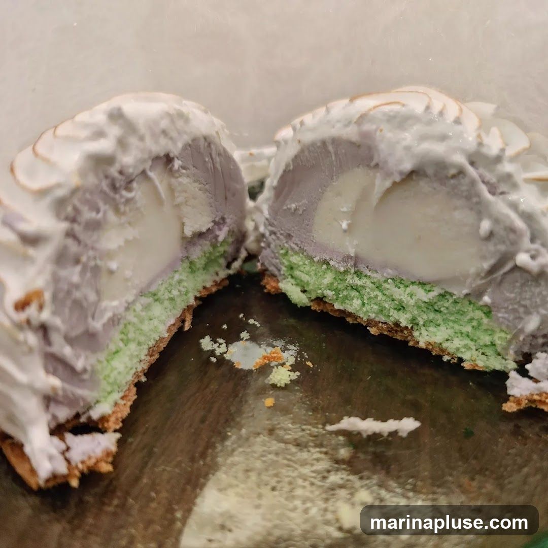 A dessert, cut in half, revealing layers of green cake, purple ice cream, and a white creamy center, all topped with meringue.
