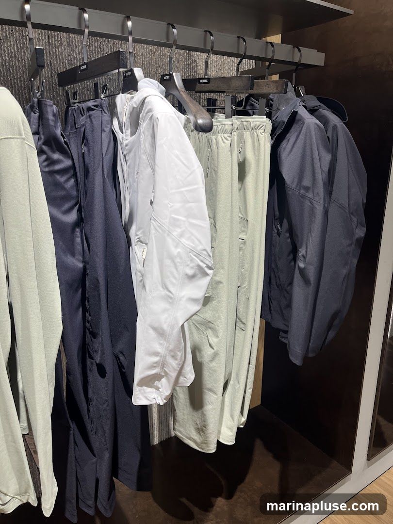 A rack of clothing, including jackets, pants, and shirts, in various colors such as light green, navy blue, white, and black. The garments are displayed on hangers in what appears to be a retail store setting.