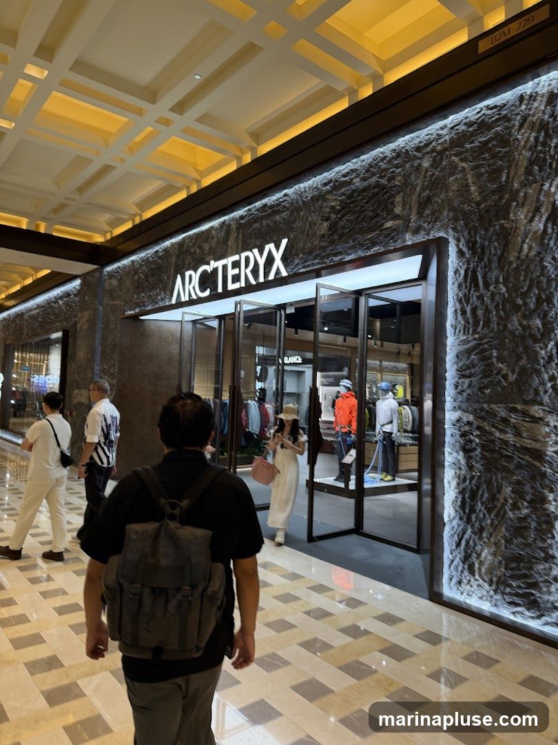 The exterior of an Arc'teryx store with the brand name prominently displayed above the entrance. The facade features a textured stone-like material. Inside, mannequins are dressed in outdoor apparel.