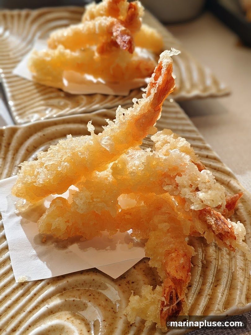 Close-up of several pieces of shrimp tempura served on textured square plates. The tempura is golden brown and crispy, with visible shrimp tails. The plates have a wavy, ridged pattern. A timestamp in the lower right corner reads 'Singapore 07/05/2025, 17:56'.