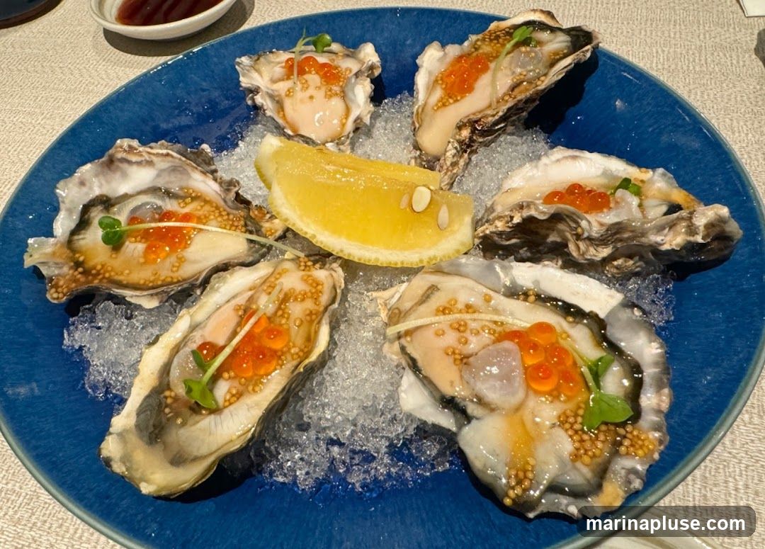 A close-up shot of six oysters served on a bed of crushed ice on a blue plate. Each oyster is garnished with bright orange salmon roe and a sprig of microgreens. A slice of lemon is placed in the center of the plate. A small dish with a dark sauce is visible in the upper left corner.