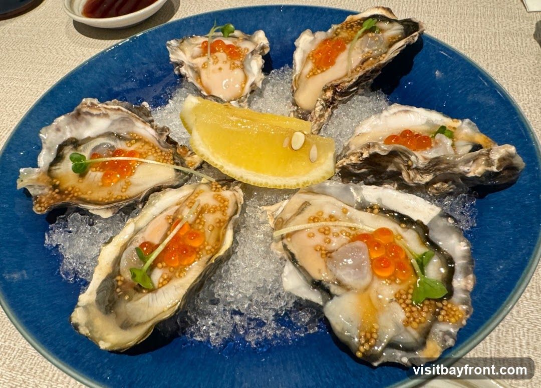 A close-up shot of six oysters served on a bed of crushed ice on a blue plate. Each oyster is garnished with bright orange salmon roe and a sprig of microgreens. A slice of lemon is placed in the center of the plate. A small dish with a dark sauce is visible in the upper left corner.