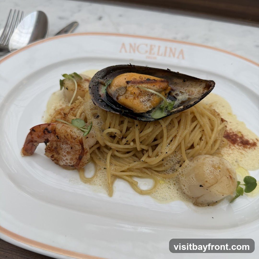 A plate of spaghetti topped with a mussel, shrimp, and scallops, served with a foamy sauce. The plate has the word "ANGELINA" printed on the rim.