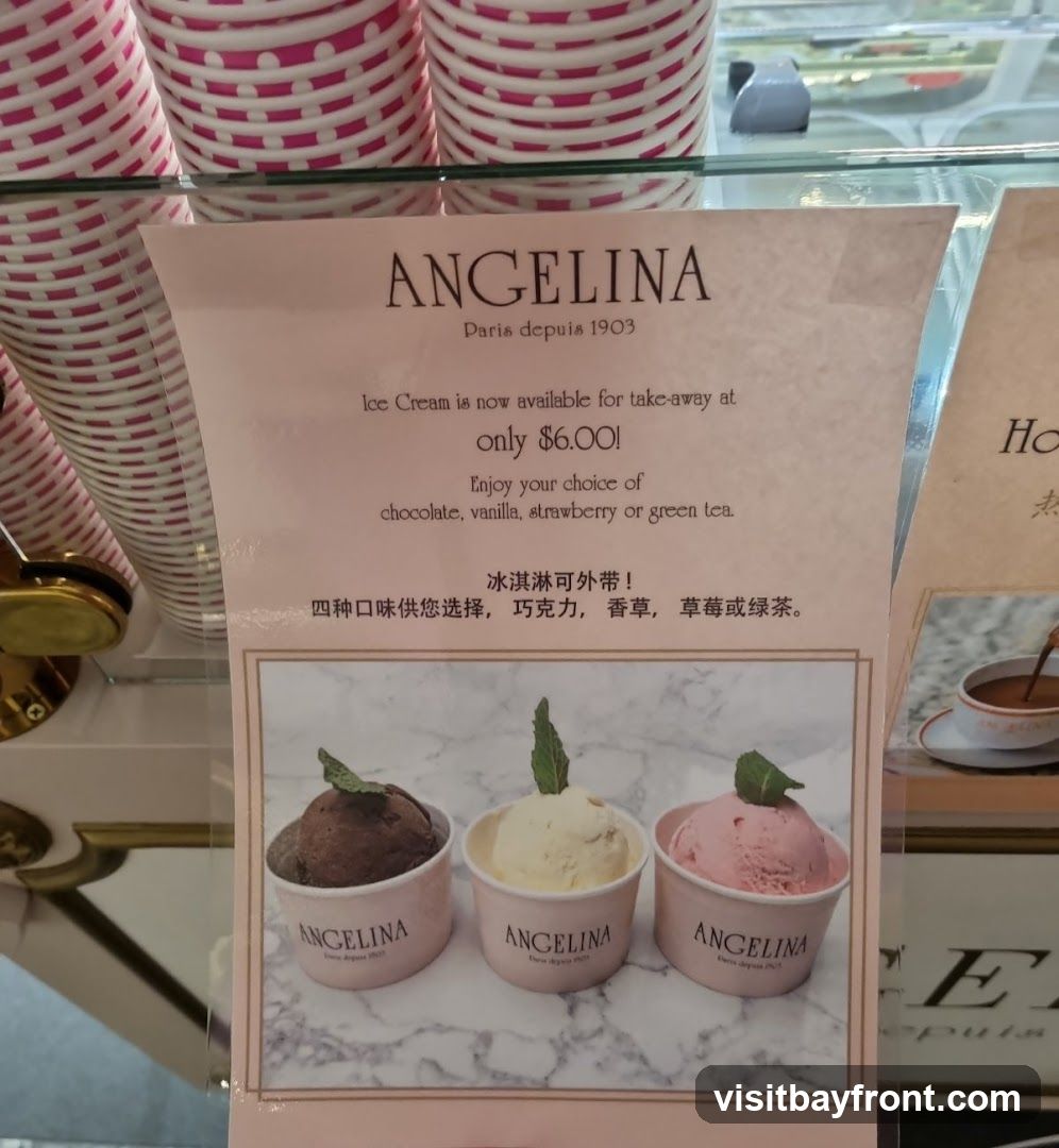A sign advertising Angelina ice cream for take-away. The sign features the Angelina logo and text stating that ice cream is available for take-away at $6.00. Customers can choose from chocolate, vanilla, strawberry, or green tea flavors. Below the text, there are three cups of ice cream: chocolate, vanilla, and strawberry.