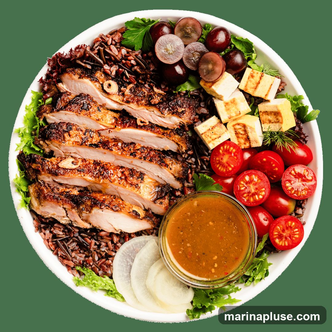 A top-down view of a white bowl filled with a meal. The bowl contains sliced grilled chicken, wild rice, halved cherry tomatoes, sliced radishes, grilled tofu cubes, and grapes. A small glass bowl of dressing is also present. The meal is garnished with lettuce and parsley.