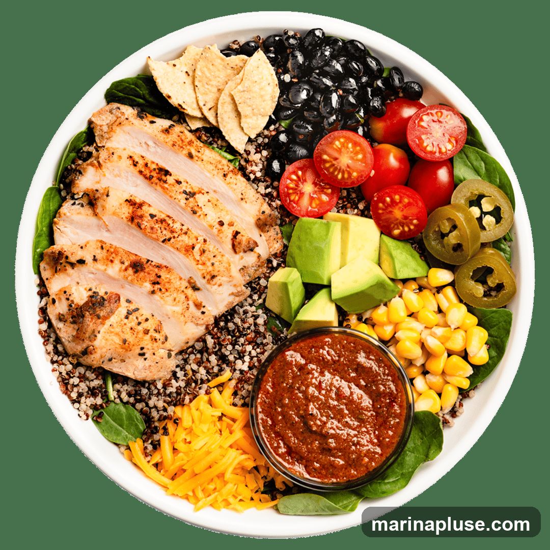 A top-down view of a chicken quinoa bowl. The bowl contains sliced grilled chicken breast, quinoa, black beans, cherry tomatoes, avocado, corn, shredded cheese, jalapeño slices, tortilla chips, and a side of salsa.