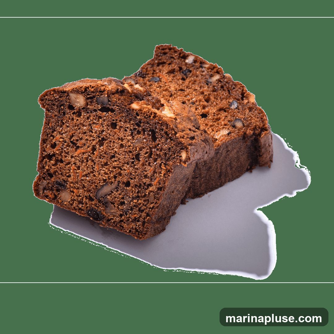 Two slices of moist carrot cake, studded with walnuts and raisins, are presented on a white surface against a black background. The cake has a rich, dark brown crumb with visible shreds of carrot and pieces of nuts.