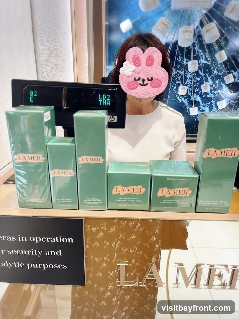 A display of La Mer skincare products, including lotions, serums, and creams, arranged on a counter. A person with a bunny sticker covering their face stands behind the counter, near a cash register. A sign stating "Cameras in operation for security and analytic purposes" is visible.