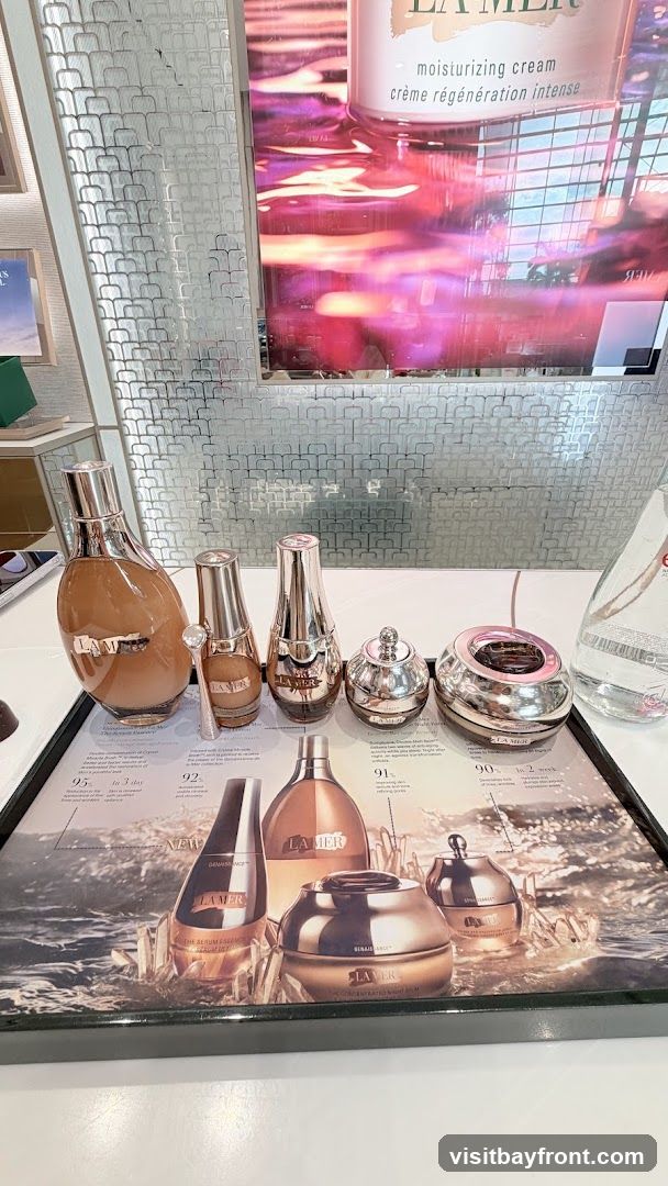 A display of La Mer skincare products, including bottles and jars, arranged on a tray with promotional imagery. A large advertisement for La Mer moisturizing cream is visible in the background.