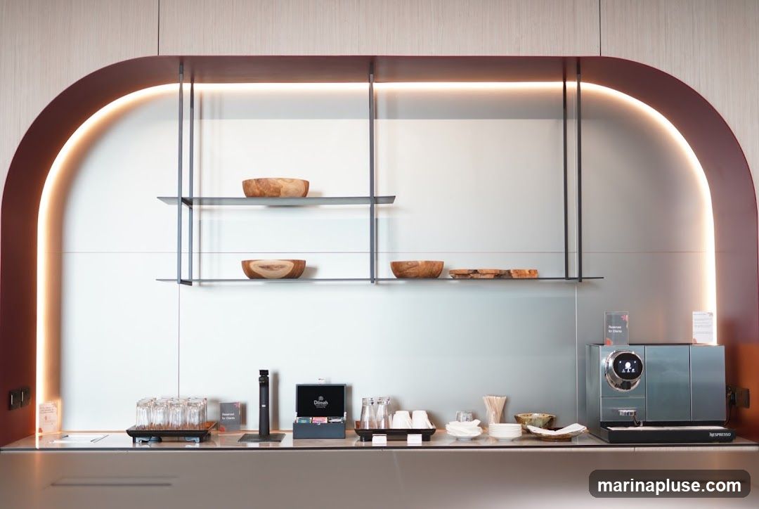A modern coffee and tea station with a Nespresso machine, a selection of tea boxes, glasses, cups, and wooden bowls. There are also small snacks on a shelf.