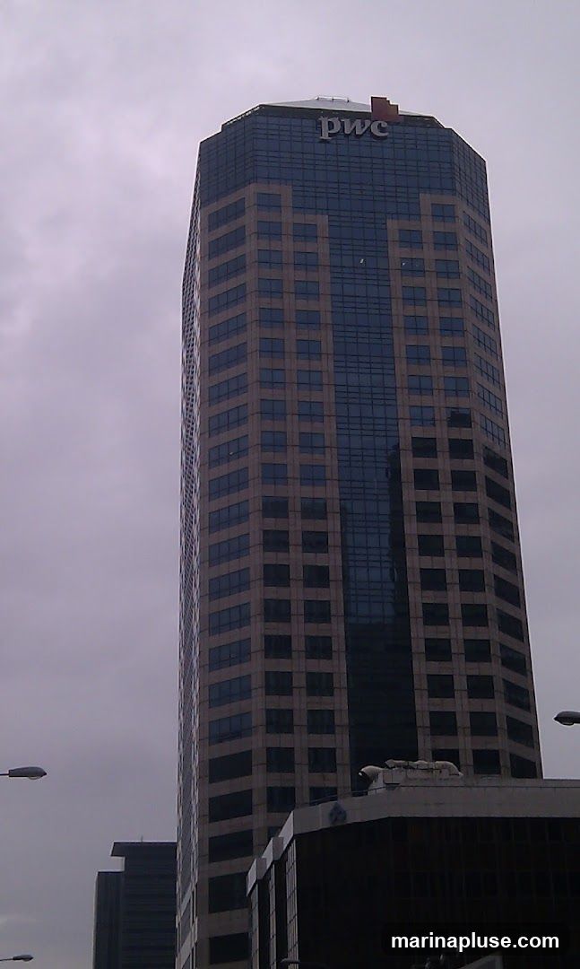 A tall, octagonal skyscraper with a glass and stone facade. The PwC logo is visible at the top of the building. The sky is overcast.