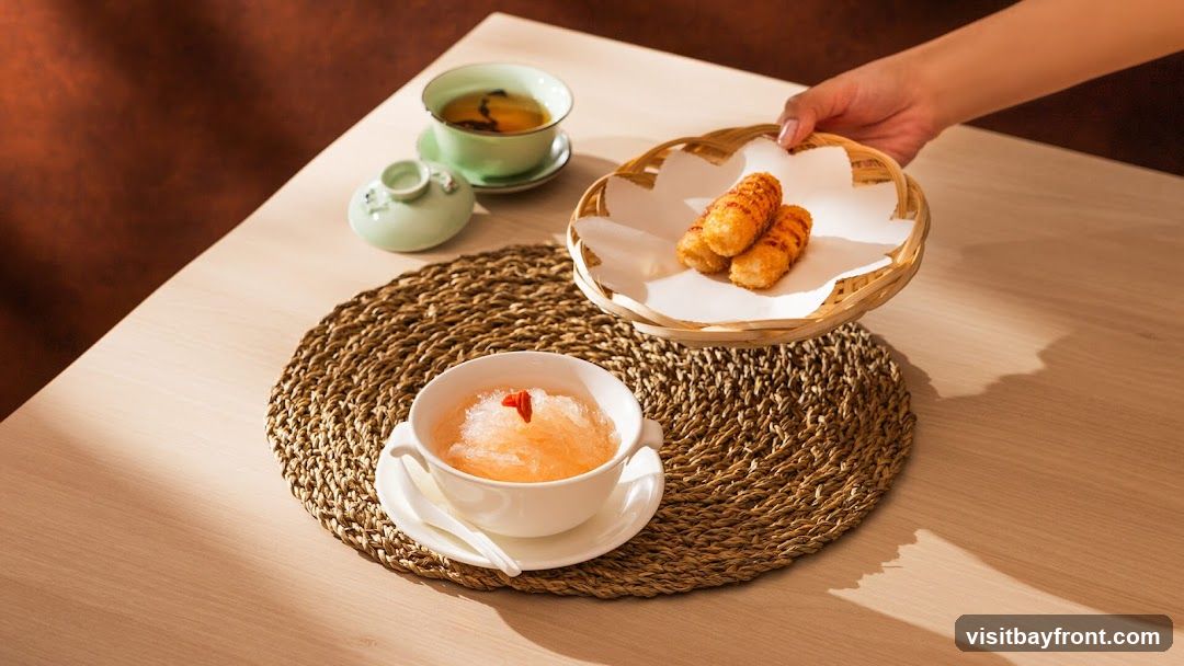 A hand is serving a basket of fried snacks to a table set with a bowl of shaved ice dessert and a cup of tea.