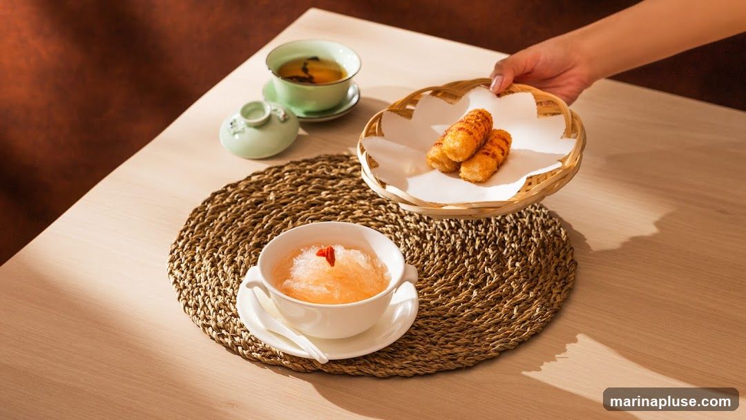 A hand is serving a basket of fried snacks to a table set with a bowl of shaved ice dessert and a cup of tea.