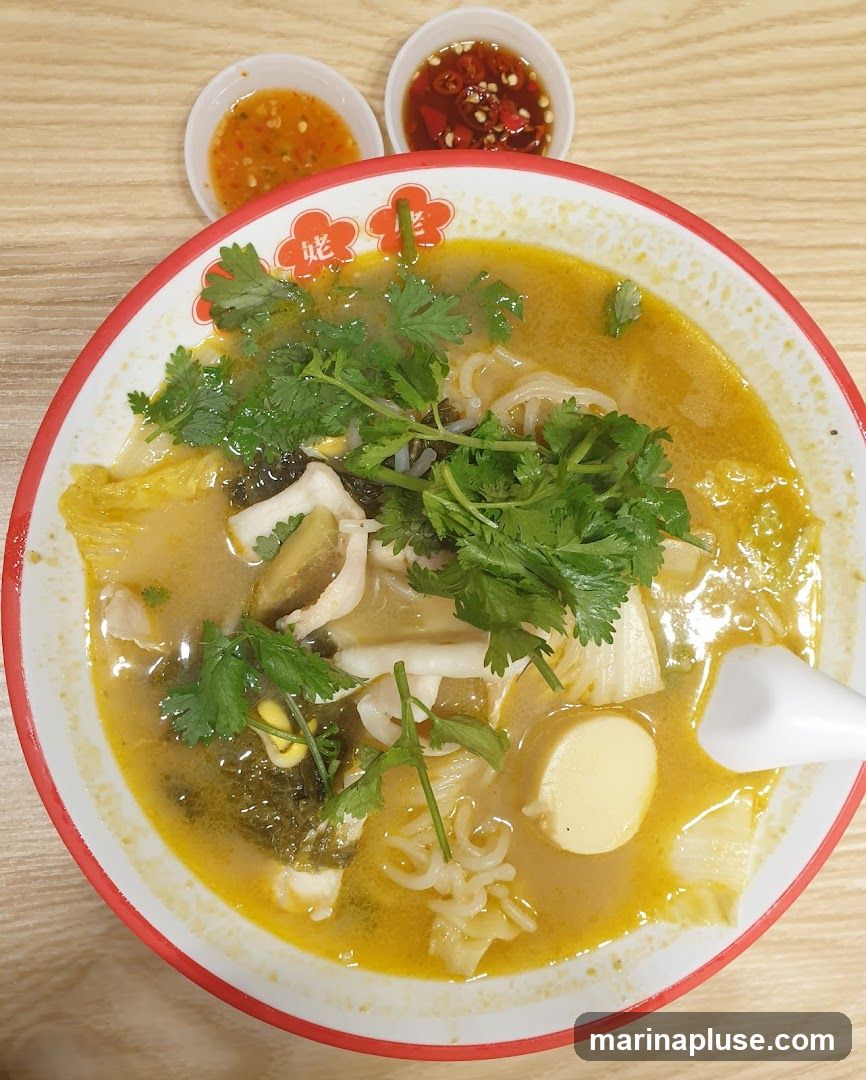 A bowl of fish soup noodles with cilantro, tofu, and pickled vegetables. Two small dipping sauces are on the side.