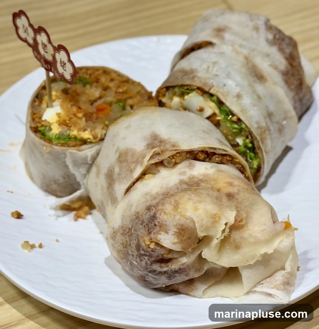 Two spring rolls on a white plate. One is cut in half, revealing the filling of rice, egg, and vegetables. A small decorative pick with Chinese characters is inserted into the cut spring roll.
