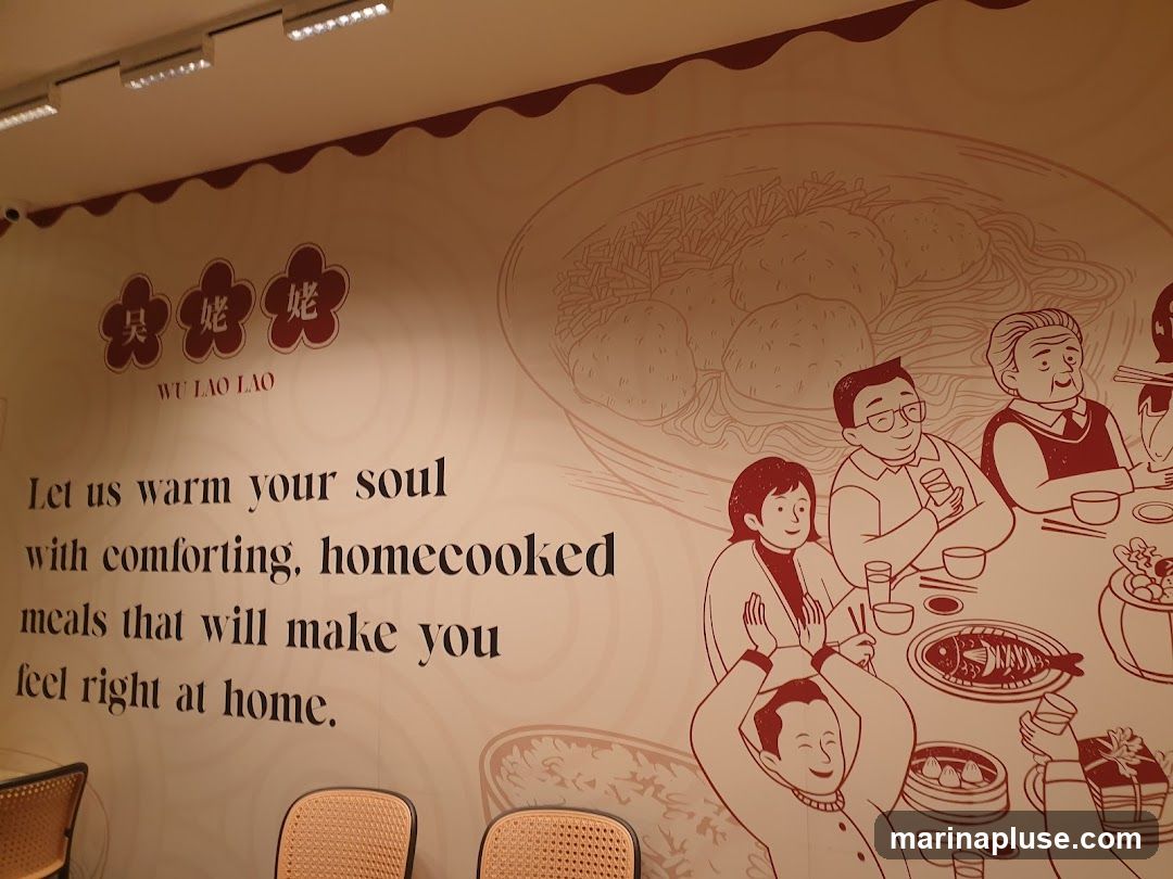 A mural on a wall depicts a family enjoying a meal. The mural features the text "WU LAO LAO" and the slogan "Let us warm your soul with comforting, homecooked meals that will make you feel right at home." The illustration shows people gathered around a table laden with food, including a whole fish, dumplings, and bowls of noodles.