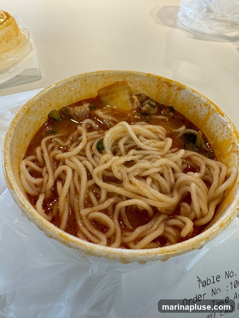 A close-up shot of a bowl of noodle soup with meat and vegetables. A receipt is visible at the bottom right corner.
