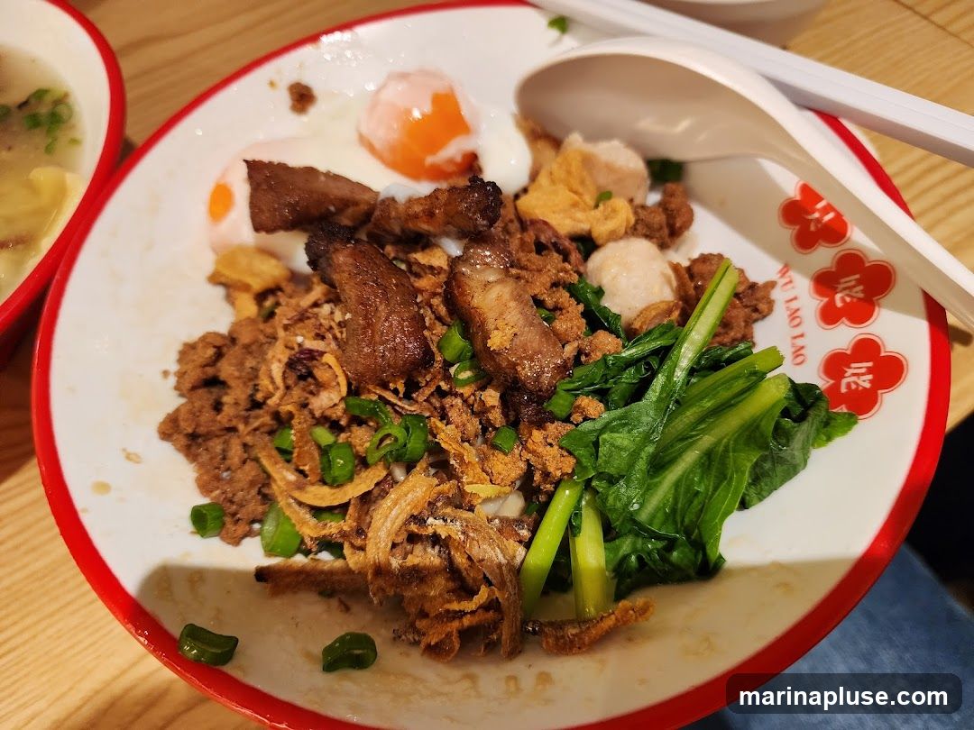 A close-up shot of a bowl of noodles topped with minced meat, sliced pork, two soft-boiled eggs, and green vegetables. Fried shallots and chopped scallions are sprinkled over the dish. A white spoon and chopsticks rest on the side of the bowl. The bowl has a red rim and a floral pattern with Chinese characters that read "WU LAO LAO". Another bowl with soup is visible in the upper left corner.