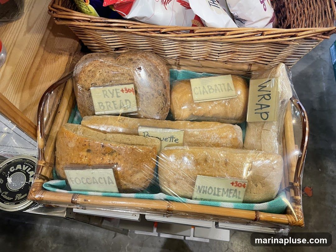 A woven basket filled with various types of bread, each individually wrapped in plastic. Labels indicate 'Rye Bread', 'Ciabatta', 'Wrap', 'Baguette', 'Focaccia', and 'Wholemeal'. Some labels have additional pricing information. A can of caviar is visible to the left.