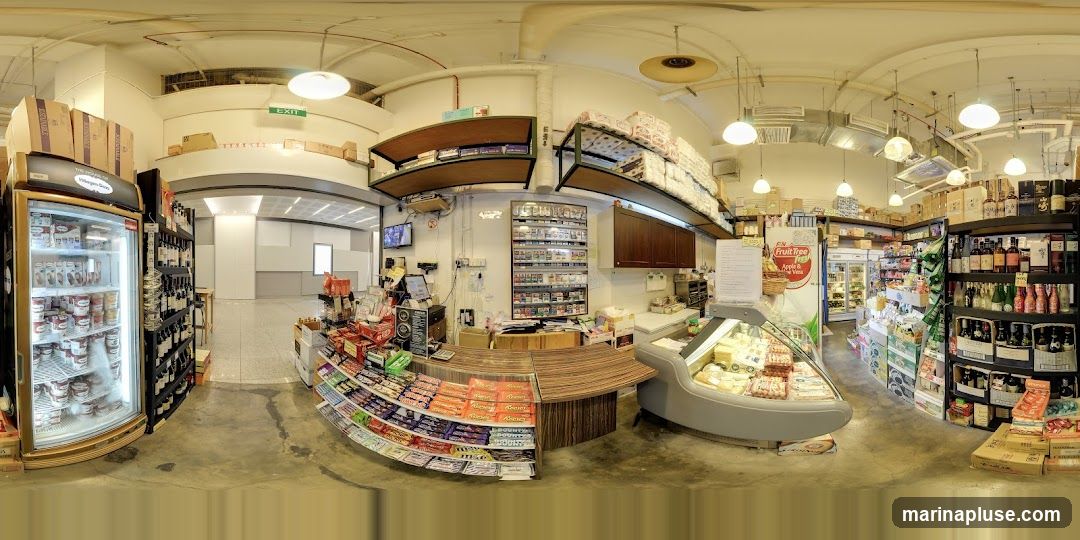 The image shows the interior of a convenience store with various products on display. In the foreground, there is a refrigerated display case filled with food items, and a counter with shelves stocked with candy bars and snacks. Behind the counter, there are shelves displaying cigarettes, and a refrigerator. To the left, a large glass-door refrigerator is filled with ice cream. To the right, shelves are stocked with bottles of wine and other beverages. Boxes of products are stacked on shelves and on the floor throughout the store. An 'EXIT' sign is visible in the background.