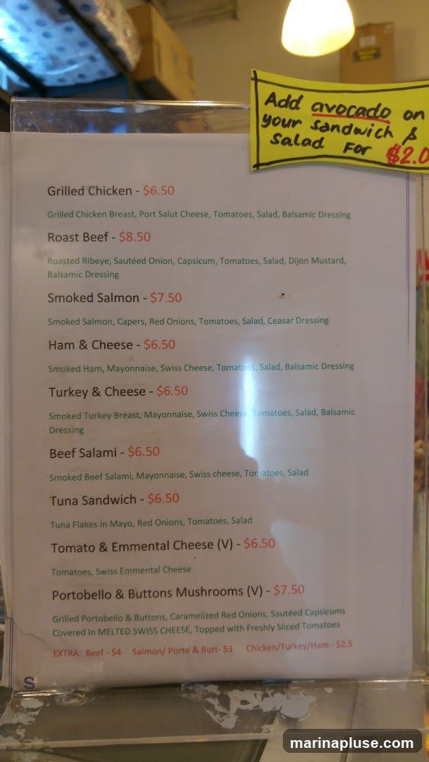 A menu board displaying various sandwich and salad options with prices. An additional note indicates that avocado can be added to sandwiches and salads for $2.0.