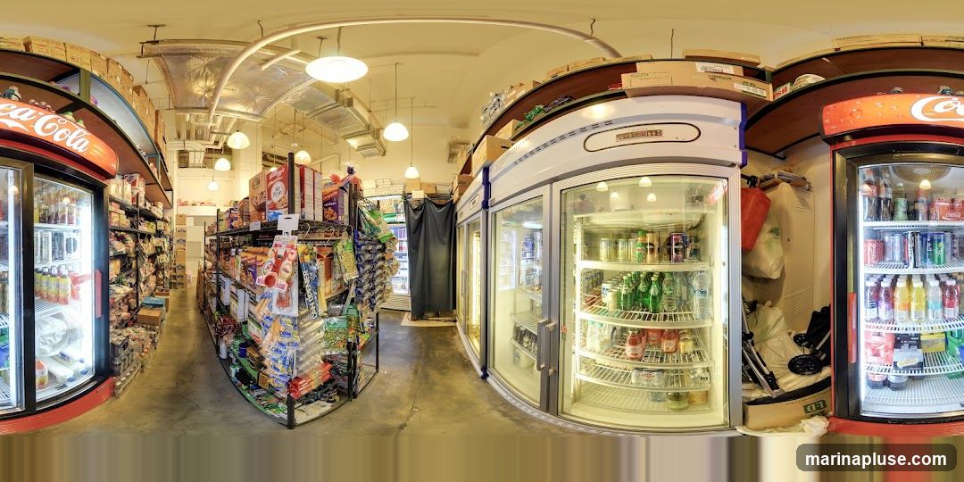 A panoramic view of the interior of a convenience store. Shelves are stocked with various food items, snacks, and drinks. Refrigerated display cases line the walls, filled with beverages. Boxes are stacked on shelves above the displays.