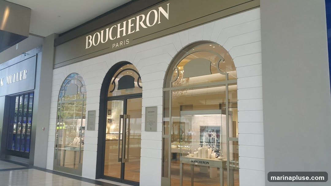 The exterior of a Boucheron Paris jewelry store. The storefront features large glass windows and doors, with arched architectural details above the entrances. The Boucheron Paris logo is prominently displayed above the entrance. Inside, display cases showcase jewelry and watches. To the left, a Franck Muller store is visible.