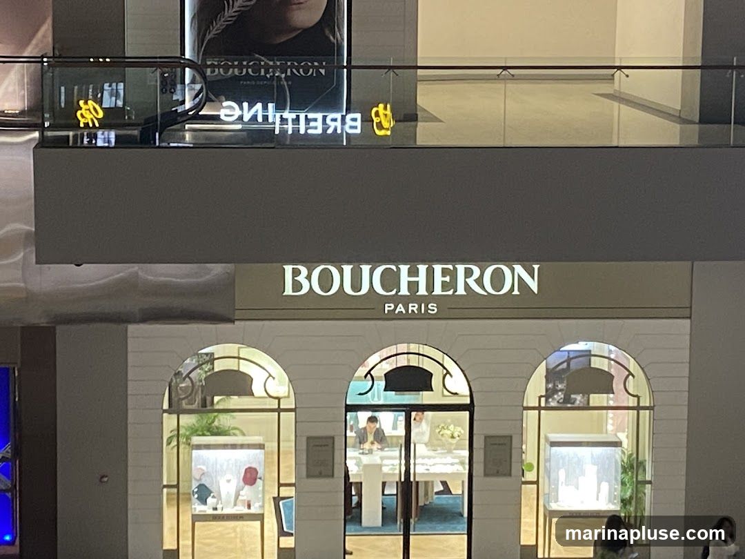 The exterior of a Boucheron Paris jewelry store. The store has a white facade with arched windows and doorways. Inside, display cases showcase jewelry. The Boucheron Paris logo is visible above the entrance.