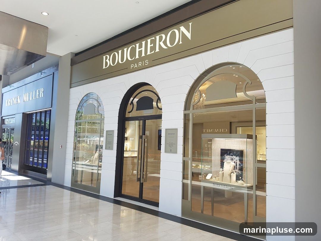 The exterior of a Boucheron Paris jewelry store. The store has a white facade with arched windows and a large sign above that reads "BOUCHERON PARIS". Inside, display cases show jewelry and watches. To the left is a Franck Muller store.