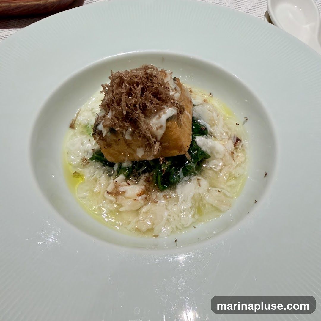 A close-up shot of a white plate holding a dish. The dish features a piece of food, possibly a quenelle or a small cake, topped with a generous amount of finely shaved truffles. This is served on a bed of wilted greens and what appears to be scrambled eggs or a creamy sauce, with visible pieces of seafood, likely crab meat. The dish is presented in a white, wide-rimmed bowl with a subtle ribbed texture on the rim.