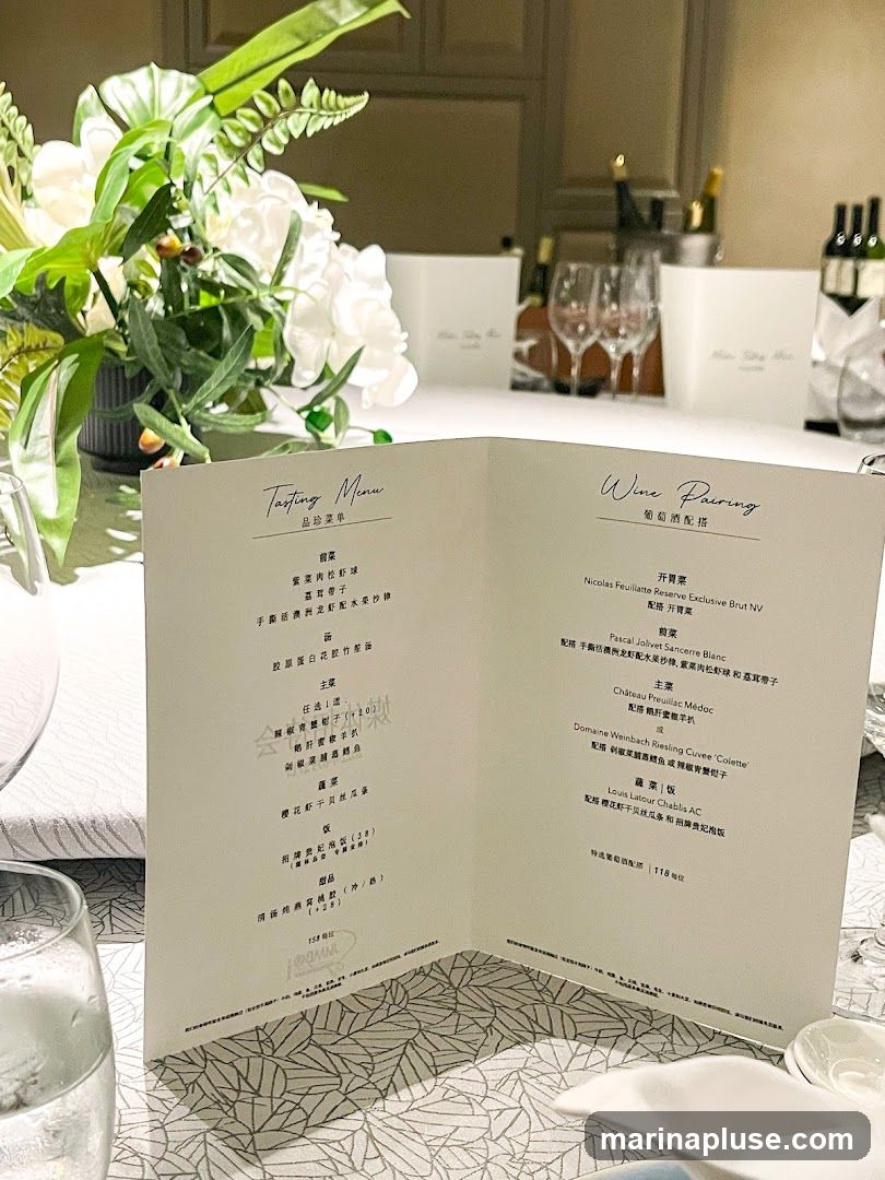 A folded menu is open on a table, with a floral arrangement to the left. The menu is divided into a Tasting Menu section and a Wine Pairing section.