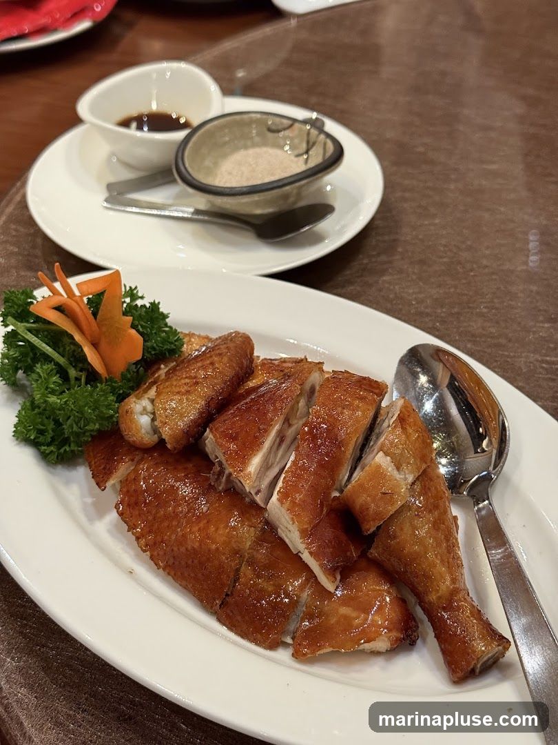 A platter of sliced roasted duck with crispy skin, garnished with parsley and a carrot flower. A small dish of dipping sauce and a dish of salt are also visible on the table.