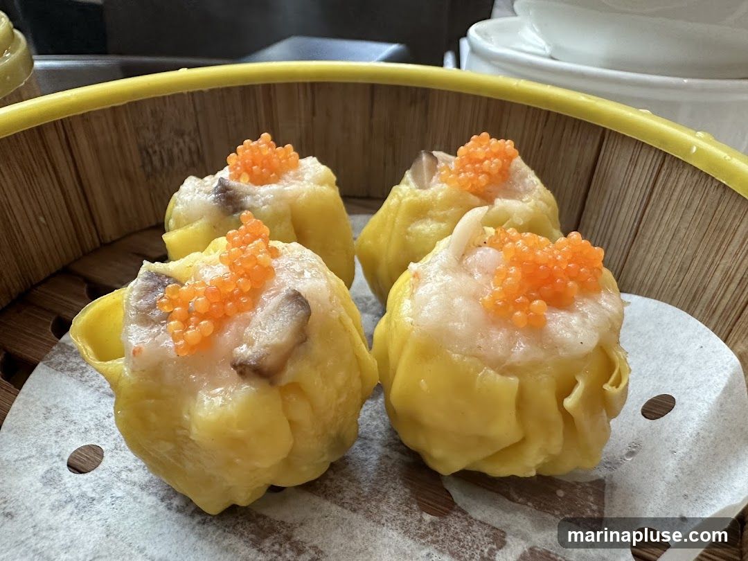 Four steamed dumplings topped with roe and mushrooms, served in a bamboo steamer basket.