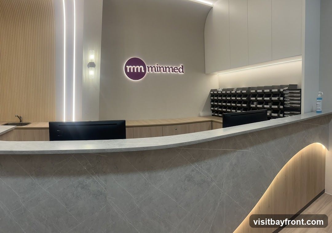A modern reception area with a marble-patterned counter. Behind the counter, there is a wall with the "minmed" logo, a sink, and a rack of mail slots. Two computer monitors are visible on the counter.