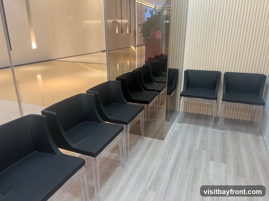 A row of black chairs with clear legs are arranged in a waiting area. The chairs are positioned against a wall with vertical wooden slats. A mirrored surface reflects more chairs and a brightly lit hallway in the background.