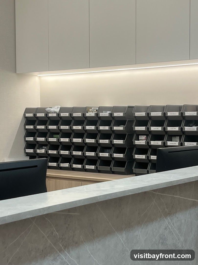 A wall of grey storage bins with labels is mounted above a wooden counter. A modern reception desk with a marble-patterned surface is in the foreground. A computer monitor is visible on the right side of the counter.