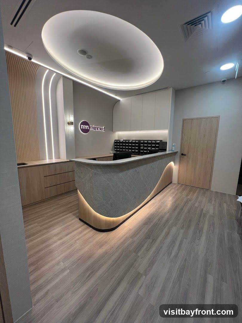 A modern reception area with a curved counter, wood-paneled walls, and soft lighting. The 'minmed' logo is visible on the wall behind the counter.